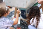 Two girls put Bondo on a boat to patch it up.