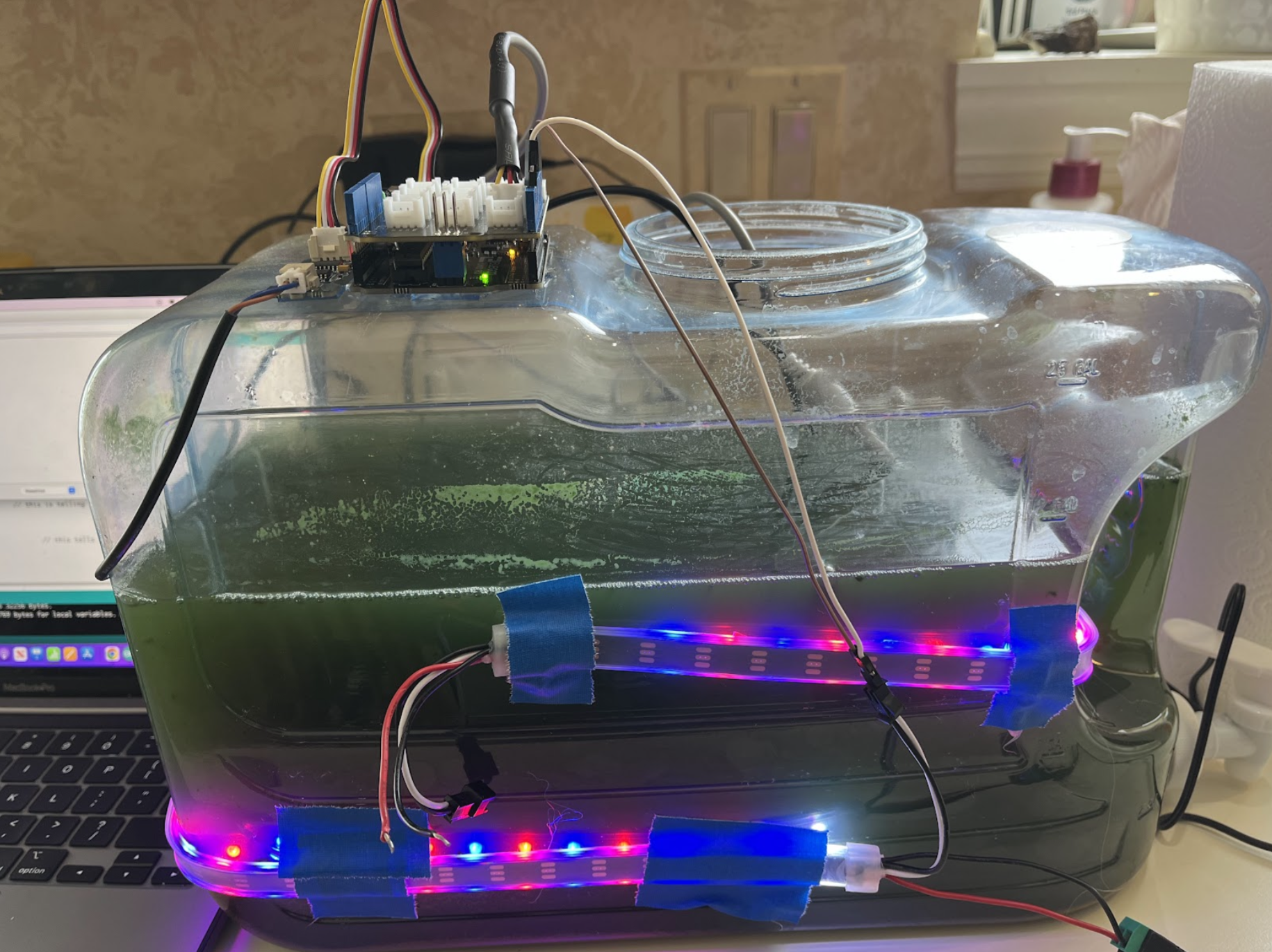 A tank of algae attached to LED lights and various sensors all monitored by a computer