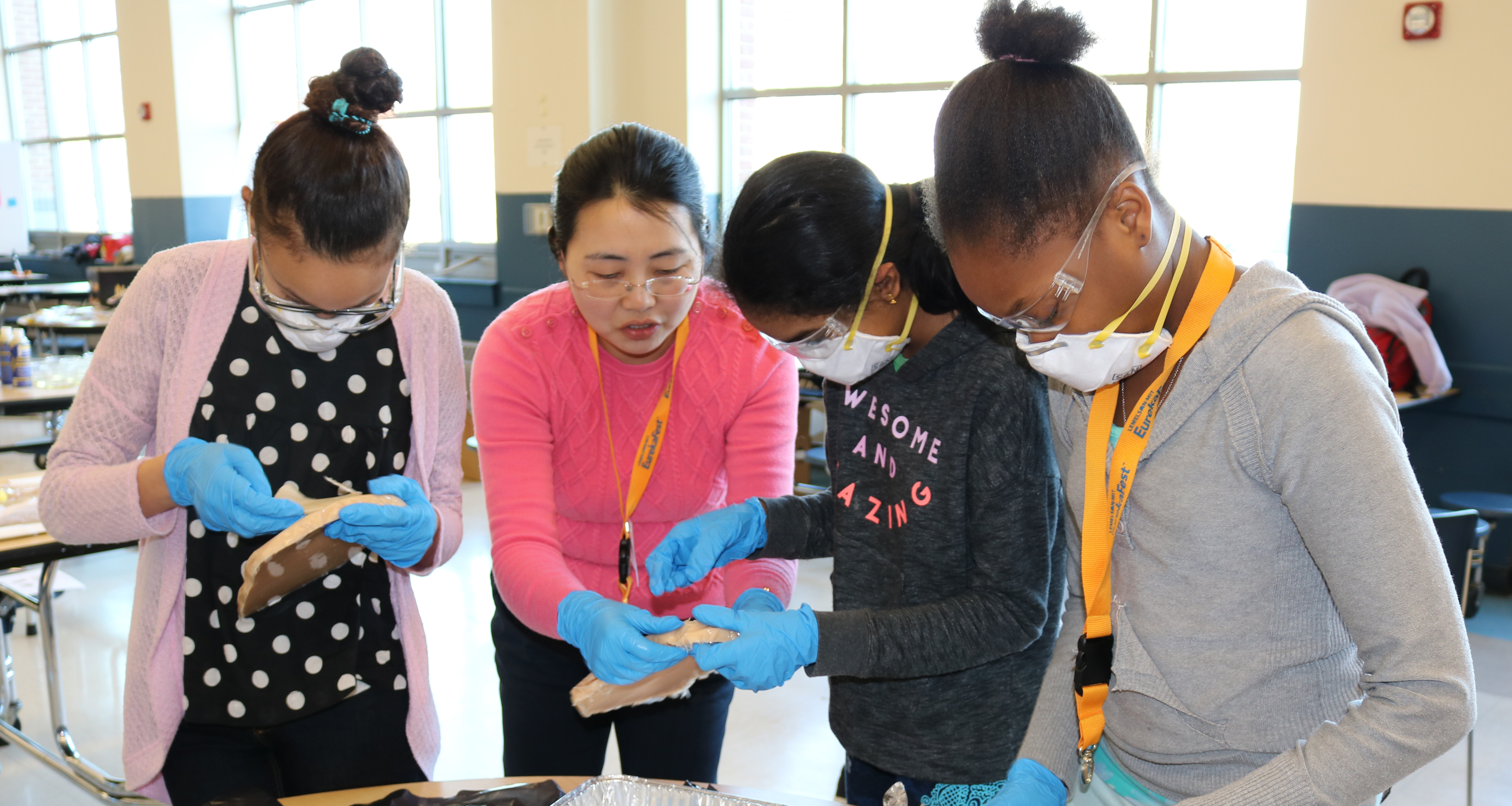 Female Teacher helping three female students on an experiment